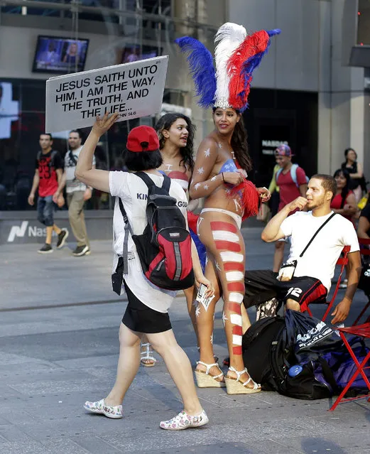In this July 28, 2015, file photo, a proselytizer walks by two women clad in thongs and body paint in Times Square, in New York. A meeting of city council members, commissioners and civic leaders was convened in New York City on Thursday, September 17, 2015, to deal with the problem of topless women and costumed panhandlers in Times Square. Although a final decision was not reached, several of those who attended said there was support for a plan to place them in a separate district zone. (Photo by Julie Jacobson/AP Photo)
