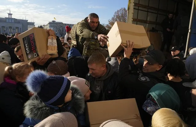 People receive humanitarian aid on central square in Kherson, Ukraine, Tuesday, November 15, 2022. Waves of Russian airstrikes rocked Ukraine on Tuesday, with authorities immediately announcing emergency blackouts after attacks from east to west on energy and other facilities knocked out power and, in the capital, struck residential buildings. (Photo by Efrem Lukatsky/AP Photo)