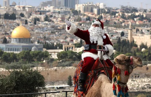 Palestinian Issa Kassissieh, dressed as Santa Claus, poses for a picture as he rides a camel at the Mount of Olives in Jerusalem, a few weeks before the upcoming holiday of Christmas on December 6, 2022. In Jerusalem's Old City there are dozens of churches, but as Christmas beckons there is just one Santa Claus, or Father Christmas – a towering Palestinian former basketball player. Each December, the streets sparkle green and red as Christian pilgrims and others arrive to celebrate Christmas in Israeli-annexed east Jerusalem. (Photo by Ahmad Gharabli/AFP Photo)