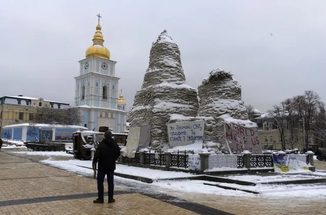 A man looks at St. Michael Cathedral standing near a monument to Princess Olga covered with sand bags to protect it from the Russian shelling, with placards displayed near the monument calling to support Ukraine, in central Kyiv, Ukraine, Monday, December 12, 2022. Ukraine has been fighting with the Russian invaders since Feb. 24 for over nine months. (Photo by Efrem Lukatsky/AP Photo)