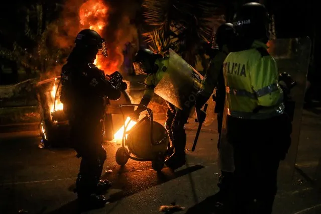 Police officers attempt to extinguish fire from a burning dumpster during a protest after a man, who was detained for violating social distancing rules, died from being repeatedly shocked with a stun gun by officers, according to authorities, in Bogota, Colombia on September 10, 2020. (Photo by Luisa Gonzalez/Reuters)