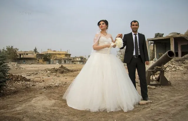 A groom holds his bride's hand as they pose near a mortar and damaged buildings before heading to their wedding ceremony in the northern Syrian town of Kobani, October 23, 2015. This Kurdish couple is the first to have a civil marriage after the town was captured from Islamic State by Kurdish-led forces and it was declared part of the system of autonomous self government established by the Kurds. (Photo by Rodi Said/Reuters)
