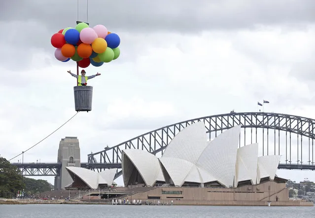 A ballon escapes as Opera Australia artistic director Lyndon Terracini rides in a garbage can under a balloon canopy over Sydney Harbour as he stands in for the character Parpignol during a test run of the prop for Puccini's La Boheme opera in Sydney, Tuesday, March 6, 2018. The production of La Boheme is set in a wintery 1960s Parisian landscape and opens on March 23. (Photo by Rick Rycroft/AP Photo)