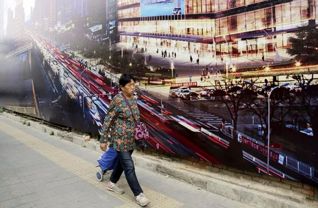 A woman walks past the advertising poster of an office building under construction in central Beijing, China, October 16, 2015. (Photo by Jason Lee/Reuters)