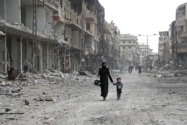 A Syrian woman and child walk down a destroyed street as civilians and rebels prepare to evacuate one of the few remaining rebel-held pockets in Arbin, in Eastern Ghouta, on the outskirts of the Syrian capital Damascus, on March 24, 2018. Syrian rebels and civilians prepared on March 24 to evacuate the penultimate opposition-held pocket of Eastern Ghouta, as the government moved ever closer to securing the outskirts of the capital. (Photo by Abdulmonam Eassa/AFP Photo)