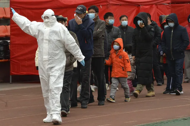 A worker wearing a protective suit gestures to a line of people at a COVID-19 testing site in Tianjin, China, Saturday, November 21, 2020. China is starting mass testing on 3 million people in a section of the northern city of Tianjin and has tested several thousand others in a hospital in Shanghai after the discovery of a pair of cases there. (Photo by Chinatopix via AP Photo)