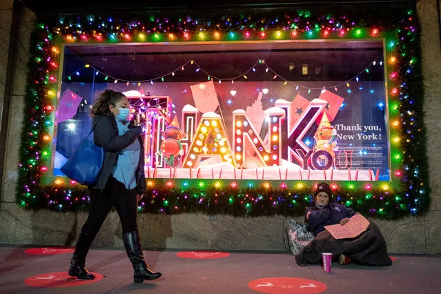 A woman wearing a mask walks near a homeless veteran sitting in front of the newly unveiled holiday windows at Macy's Herald Square on November 21, 2020 in New York City. (Photo by Alexi Rosenfeld/Getty Images)