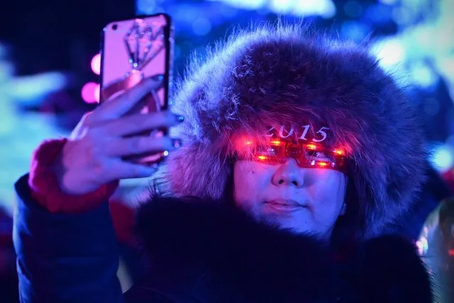 A woman uses her mobile phone to take a photo during the New Year's Eve countdown event in front of Beijing's National Stadium, Known as the Bird's Nest in Beijing on December 31,2014. Beijing is bidding to host the 2022 Winter Olympic Games, with a decision on the winning city to be made in July 2015. (Photo by Wang Zhao/AFP Photo)