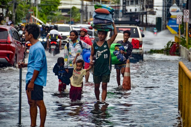 Residents carrying their belongings, wade through a flooded street in Mandaue City, Cebu province on November 4, 2025, after Typhoon Kalmaegi hit overnight. Residents sought refuge on rooftops and cars floated through flooded streets on November 4 as Typhoon Kalmaegi battered the central Philippines, leaving at least two people dead. (Photo by Alan Tangcawan/AFP Photo)
