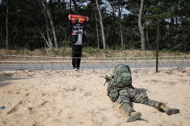 An anti-war activist holds up a sign “Stop war exercise, Go home” in front of a South Korean marine taking a position during a U.S and South Korea marine corps combined amphibious landing drill called the “Ssangyong” exercise, in Pohang, South Korea on March 29, 2023. (Photo by Kim Hong-Ji/Reuters)