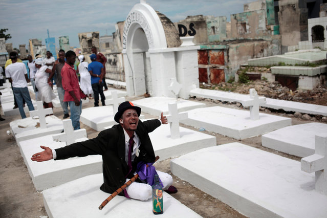 A voodoo believer, dressed as “Gede”, a spirit of voodoo, greets people (not pictured) as he sits on a grave during celebrations at the cemetery of Port-au-Prince, Haiti, November 1, 2016. (Photo by Andres Martinez Casares/Reuters)