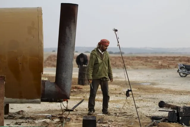 Yousef Ayoub, 34, works at a makeshift oil refinery site in Marchmarin town, southern countryside of Idlib, Syria December 16, 2015. (Photo by Khalil Ashawi/Reuters)
