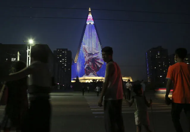 North Koreans watch light show projected on the pyramid-shaped Ryugyong Hotel, in Pyongyang, North Korea, Friday, July 27, 2018. The light show was part of the commemoration of the 65th anniversary of the end of the Korean War, which the country celebrates as the day of “victory in the fatherland liberation war”. (Photo by Dita Alangkara/AP Photo)