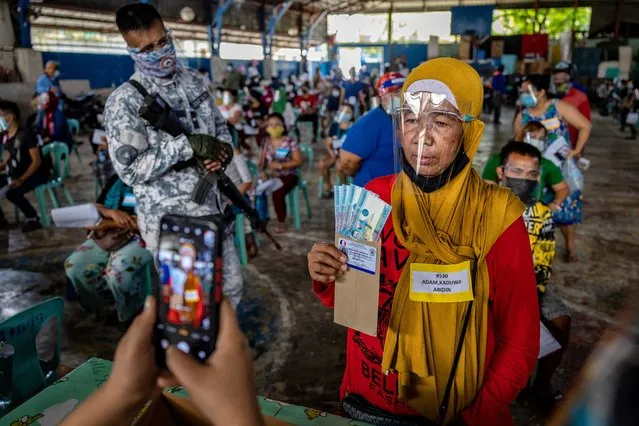 A social worker takes a picture of a resident receiving cash aid on April 7,2021 in Manila, Philippines. Each resident is entitled to 1,000 pesos ($20), with a limit of 4,000 pesos ($80) per household. Some 24 million people in Manila and nearby provinces remain under strict lockdown, the longest in the world, as the worst COVID-19 surge in Southeast Asia continues to hammer the country's healthcare system. The Philippines has confirmed more than 813,000 cases of COVID-19 so far, with nearly one in four people being tested turning out positive. (Photo by Ezra Acayan/Getty Images)