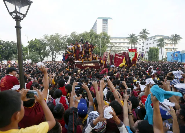 Catholic devotees take photos and wave towels as a procession of the image of the Black Nazarene passes by in a raucous procession to celebrate its feast day in Manila, Philippines, Saturday, January 9, 2016. (Photo by Bullit Marquez/AP Photo)