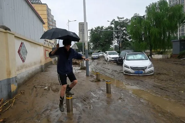 A man walks past cars stuck in mud after heavy rains in Mentougou district in Beijing on August 1, 2023. At least 11 people are dead and 27 missing after heavy rains lashed Beijing, state media said on August 1, in downpours that have submerged roads and deluged neighbourhoods with mud. (Photo by Pedro Pardo/AFP Photo)