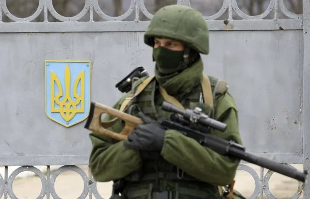In this Sunday, March 2, 2014 file photo an unidentified armed man guards the gate of Ukraine's infantry base in Privolnoye, Crimea. (Photo by Darko Vojinovic/AP Photo)