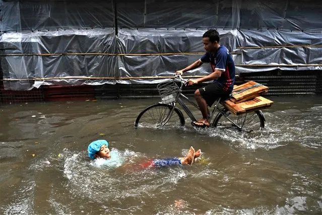 A child plays in flood waters as a youth cycles past following heavy rain in Yangon on June 28, 2023. (Photo by Sai Aung Main/AFP Photo)