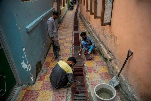 Kashmiri workers paint a mesh covering a drain inside a narrow alley in Srinagar, Indian controlled Kashmir, Sunday, August 1, 2021. (Photo by Mukhtar Khan/AP Photo)
