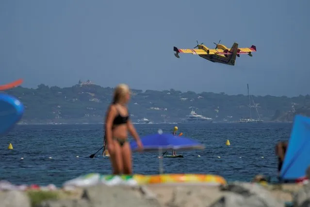 Holiday makers watch a water-dumping aircraft after it filled up its tanks with water to fight wildfires, in the bay of Sainte-Maxime, southern France, Wednesday, August 18, 2021. A wildfire near the French Riviera has killed one person and remained out of control as it raged through forests for a third day Wednesday, according to authorities. (Photo by Daniel Cole/AP Photo)