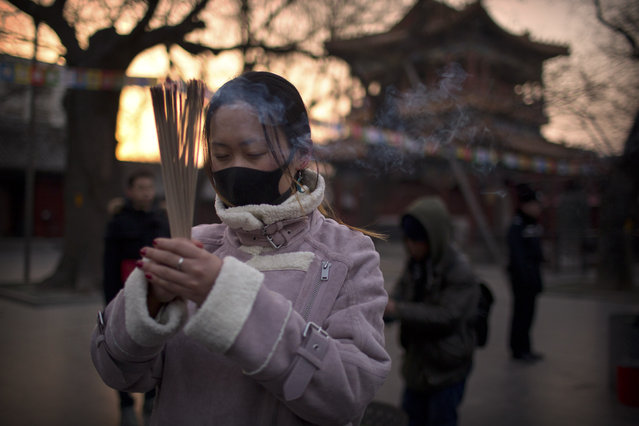 A woman holds sticks of incense as she prays at the Lama Temple in Beijing, Tuesday, February 5, 2019. Chinese people are celebrating the first day of the Lunar New Year on Tuesday, the Year of the Pig on the Chinese zodiac. (Photo by Mark Schiefelbein/AP Photo)