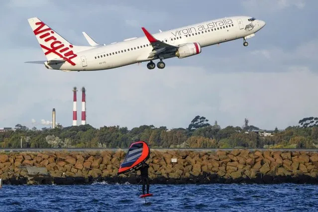 A man wing foils on Botany Bay as a passenger jet take off from Sydney Airport in Australia, Monday, September 5, 2022. (Photo by Mark Baker/AP Photo)