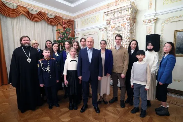 Russian President Vladimir Putin, center, and Russian Orthodox Archbishop of Odintsovo and Krasnogorsk Foma (Nikolay Mosolov), left, pose for a photo with the families of military personnel who died during the special military operation in Ukraine at the Novo-Ogaryovo state residence outside Moscow, Russia, on Saturday, January 6, 2024. (Gavriil Grigorov, Sputnik, Kremlin Pool Photo via AP Photo)