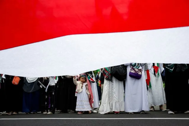 Hazra Kholid, a 3-year-old girl, peeks from under a giant Indonesian flag, during a protest urging the Egyptian government to open the Rafah border crossing to get aid delivered into Gaza, outside the Egyptian embassy in Jakarta, Indonesia on March 4, 2024. (Photo by Willy Kurniawan/Reuters)