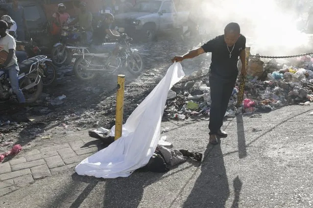 A person lifts a sheet to look at the identity of a body lying on the ground after an overnight shooting in the Petion Ville neighborhood of Port-au-Prince, Haiti, Monday, March 18, 2024. (Photo by Odelyn Joseph/AP Photo)