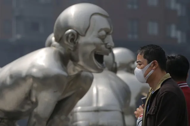 A Chinese, wearing a mask, passes by a sculpture during a smoggy day in Beijing city, China, 13 April 2016. The Chinese Ministry of Environmental Protection received about 15,000 public complaints about pollution in 2015. The air pollution tip-offs became the top 78.3 percent of all complaints received through the ministry's hotline and 68 percent through the WeChat, according to the media reports. (Photo by Wu Hong/EPA)