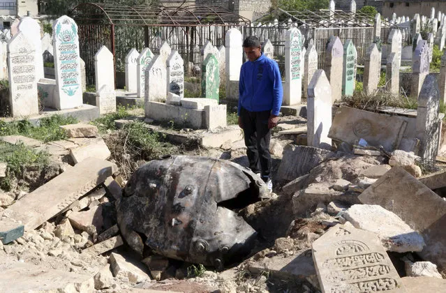 A man looks down at an unexploded barrel bomb dropped by forces loyal to Syria's President Bashar al-Assad at a cemetery in the al-Qatanah neighbourhood of Aleppo March 27, 2014. (Photo by Mahmoud Hebbo/Reuters)