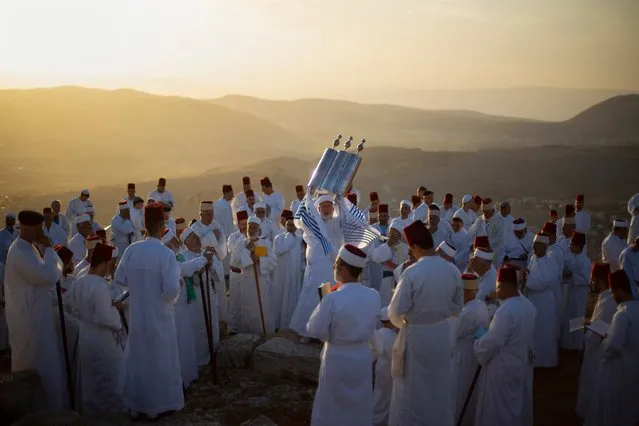 A member of the ancient Samaritan community, wrapped in a prayer shawl, holds up a Tora scroll as worshippers pray during the Passover pilgrimage at the religion's holiest site on the top Mt. Gerizim, near the West Bank town of Nablus, Sunday, May 2, 2021. Samaritans descended from the ancient Israelite tribes of Menashe and Efraim but broke away from mainstream Judaism 2,800 years ago. Today, the remaining 810 Samaritans live in the Palestinian city of Nablus in the West Bank and the Israeli seaside town of Holon, south of Tel Aviv. (Photo by Majdi Mohammed/AP Photo)