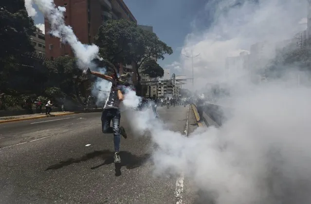 A demonstrator throws back a tear gas grenade launched by the Bolivarian National Police during a protest in Caracas, Venezuela, Saturday, April 8, 2017. Opponents of President Nicolas Maduro protest on the streets of Caracas on Saturday as part of a week-long protest movement that shows little sign of losing steam. (Photo by Fernando Llano/AP Photo)