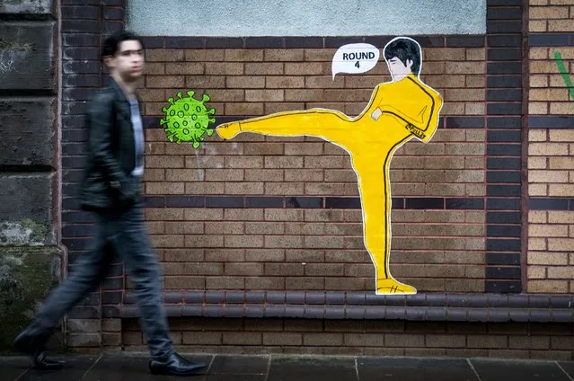 A member of the public walks past a piece of street art by “Palley” that features Bruce Lee kicking a coronavirus molecule in Glasgow's East End on Sunday, January 23, 2022. (Photo by Jane Barlow/PA Images via Getty Images)