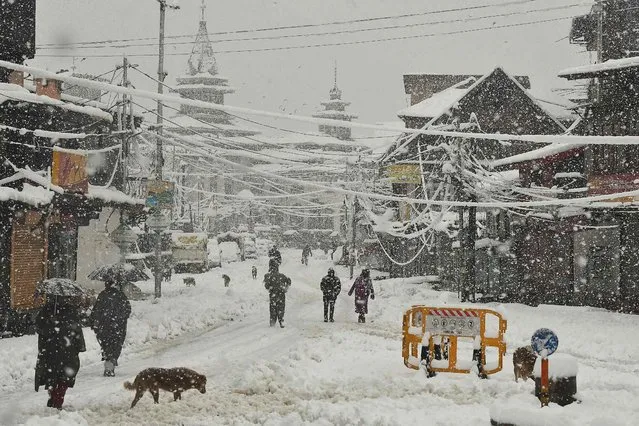 People walks along a road during a heavy snowfall in Srinagar on February 23, 2022. (Photo by Tauseef Mustafa/AFP Photo)