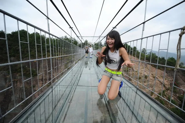 A visitor kneels on the 180-meter-high and 300 meter-long glass-bottomed suspension bridge at the Shiniuzhai National Geopark in Pingjiang county, in central China's Hunan province, 24 September 2015. (Photo by Jiao Zi/Imaginechina via AFP Photo)