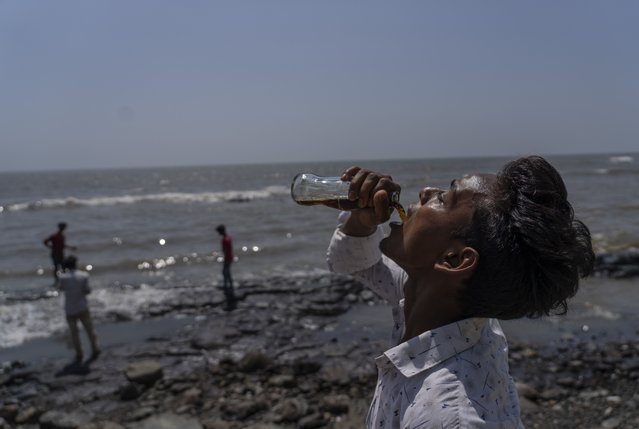 A boy drinks soda at a promenade on the Arabian Sea coast in Mumbai, India, Sunday, May 1, 2022. (Photo by Rafiq Maqbool/AP Photo)