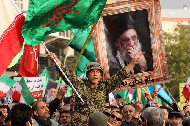 Iranians hold pictures of supreme leader Ayatollah Ali Khamenei and wave national flags during a rally to show their support to the Islamic Republic system and to condemn recent violent protests following fuel price hike in the country, in Tehran, Iran, 25 November 2019. (Photo by Abedin Taherkenareh/EPA/EFE)