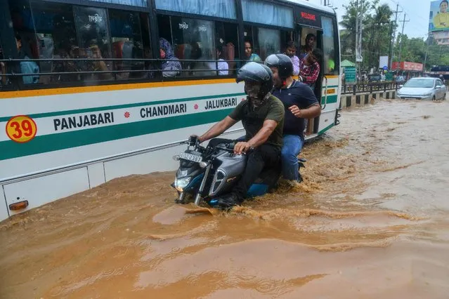Men ride a motorbike past a bus along a waterlogged road following a heavy rainfall in Guwahati on May 25, 2022. (Photo by Biju Boro/AFP Photo)