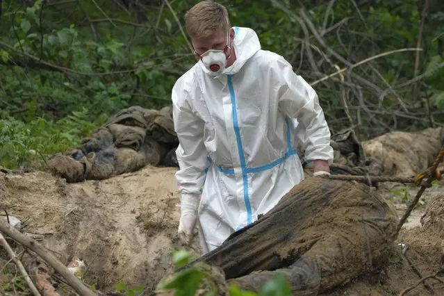 A member of an extraction crew works during an exhumation at a mass grave near Bucha, on the outskirts of Kyiv, Ukraine, Monday, June 13, 2022. (Photo by Natacha Pisarenko/AP Photo)