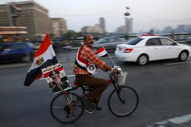 A supporter of Egyptian President Abdel-Fattah el-Sissi carries his poster on his bike as he celebrates with others for Thursday's opening of the new extension of the Suez Canal, riding on the Qasr El Nile Bridge in Cairo, Egypt, Wednesday, August 5, 2015. Egypt will unveil a major extension of the Suez Canal on Thursday, a mega-project that has emerged as a cornerstone of el-Sissi's efforts to restore national pride and revive the economy after years of unrest. (Photo by Hassan Ammar/AP Photo)