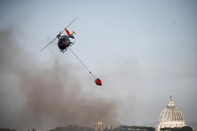 A firefighting helicopter drops water to extinguish a forest fire, with St. Peter's Basilica in the background, in north Rome, Italy on July 4, 2022. (Photo by Yara Nardi/Reuters)