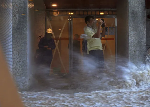 A man takes pictures against strong wind caused by typhoon Hato at a housing area in Hong Kong, Wednesday, August 23, 2017. A powerful typhoon barreled into Hong Kong on Wednesday, forcing offices and schools to close and leaving flooded streets, shattered windows and hundreds of canceled flights in its wake. (Photo by Apple Daily via AP Photo)