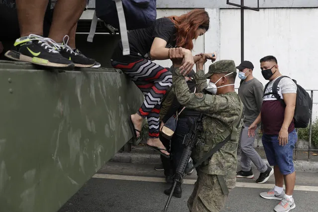 A soldier assists a woman as she goes down a military truck that offers a free ride after public transportation have been halted due to the enhanced community quarantine to prevent the spread of the new coronavirus along an almost empty hi-way in Manila, Philippines on Wednesday, March 18, 2020. The Philippine government lifted a 72-hour deadline for thousands of foreign travelers to leave the country's main northern region which has been placed under quarantine due to the growing number of coronavirus infections, officials said. (Photo by Joeal Calupitan/AP Photo)