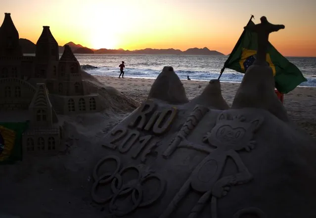 A jogger runs along Copacabana beach as a sand sculpture stands along the promenade Monday, August 1, 2016, in Rio de Janeiro, Brazil. The iconic Copacabana beach will be the starting point for the road cycling race, marathon swimming and triathlon competitions during the Olympics. (Photo by David Goldman/AP Photo)