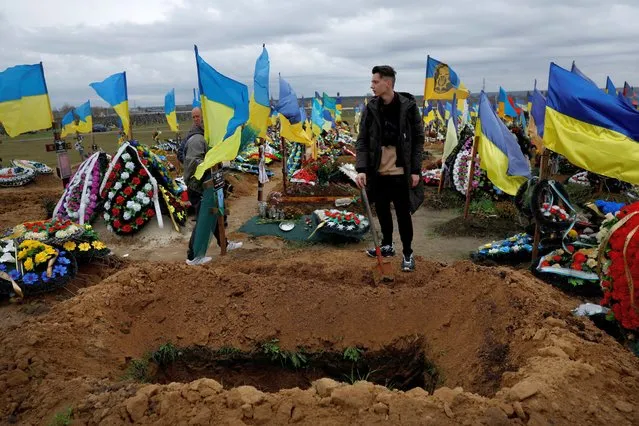 Ruslan Burmenko holds a shovel as he tidies up the grave of his brother Roman Burmenko, who died, aged 31, while helping injured soldiers during a battle in Bakhmut, next to a freshly dug grave at a soldiers' graveyard, amid Russia's invasion of Ukraine in Kharkiv, Ukraine on October 23, 2022. (Photo by Clodagh Kilcoyne/Reuters)