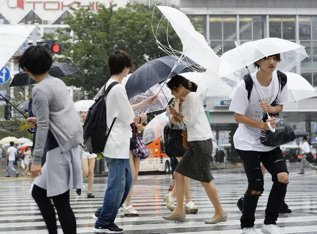People walk in a strong wind caused by Typhoon Mindulle, in Tokyo Monday, August 22, 2016. The typhoon sweeping through Tokyo and surrounding areas has forced the cancellation of more than 400 domestic flights in Japan and disrupted train service. (Photo by Akiko Matsushita/Kyodo News via AP Photo)