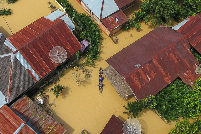 This aerial photo taken on November 5, 2022 shows people on a boat making their way through a street flooded due to torrential rains in Aceh Tamiang, Aceh province. (Photo by Zikri Maulana/AFP Photo)
