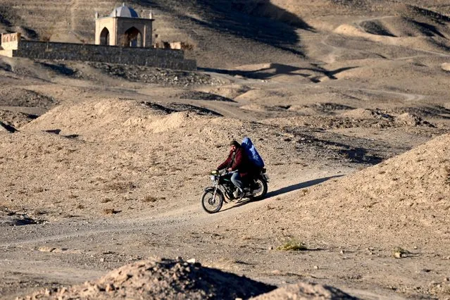 In this photo taken on November 27, 2022, people ride a motorcycle near a historic minaret along a hill in the north-east of Ghazni province. (Photo by Wakil kohsar/AFP Photo)