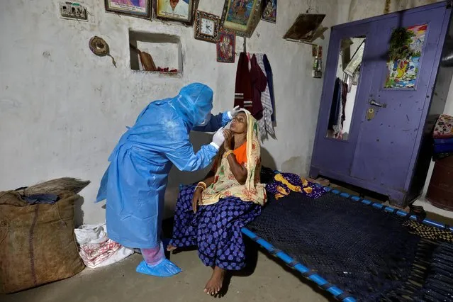 A healthcare worker wearing personal protective equipment (PPE) takes swabs from a woman in her house during a door-to-door survey for the coronavirus disease (COVID-19), amidst the spread of the disease in Khoraj village, in Gujarat, India, September 16, 2020. (Photo by Amit Dave/Reuters)